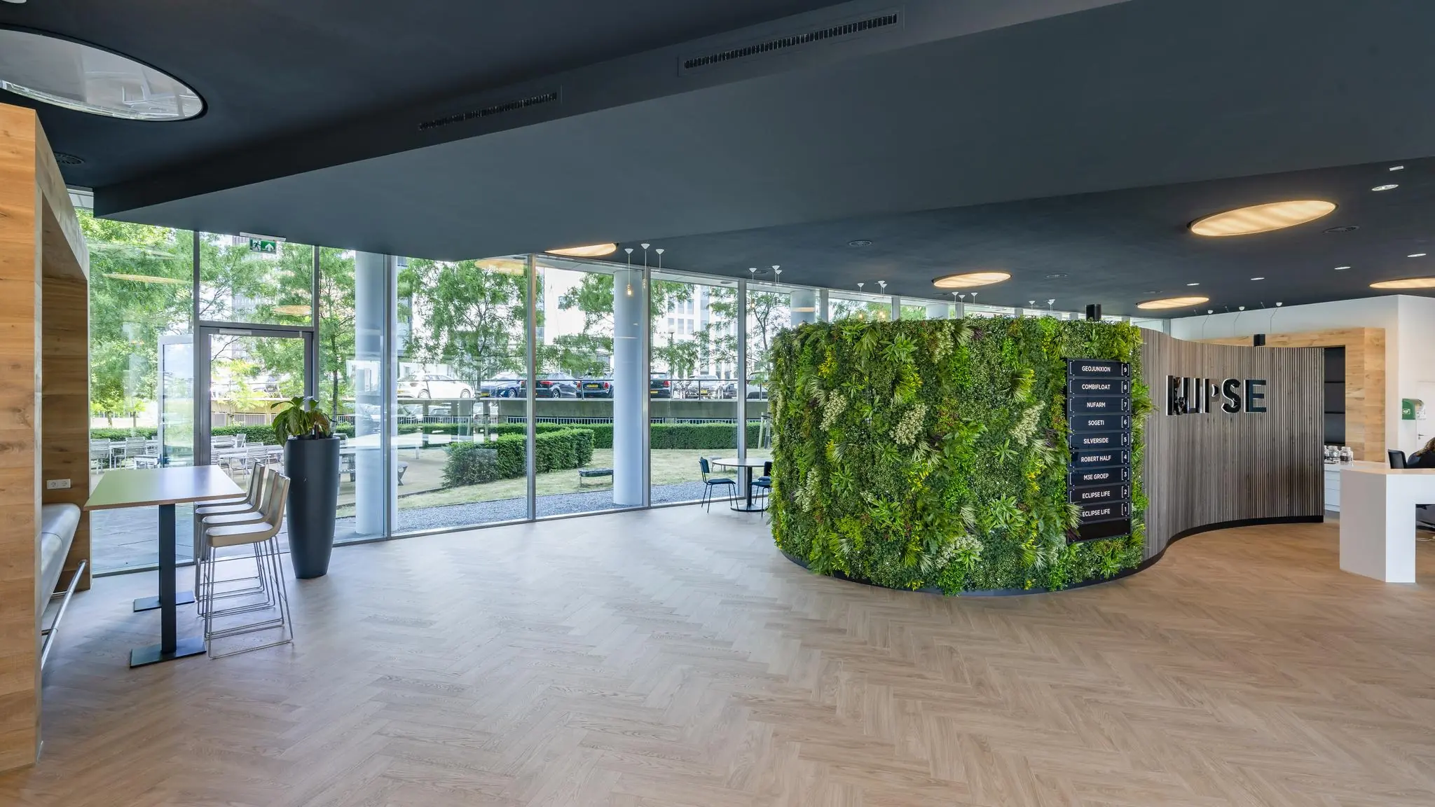 Moderne entreehal van het Rivium Quadrant met een groene plantenwand, grote ramen en een houten vloer.